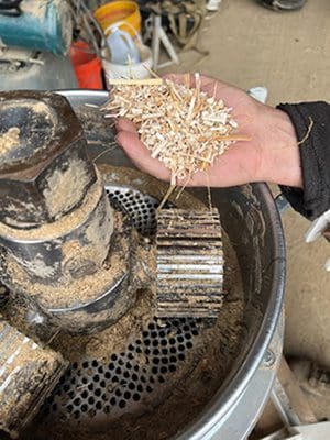 Hand holding wood shavings over grinder.