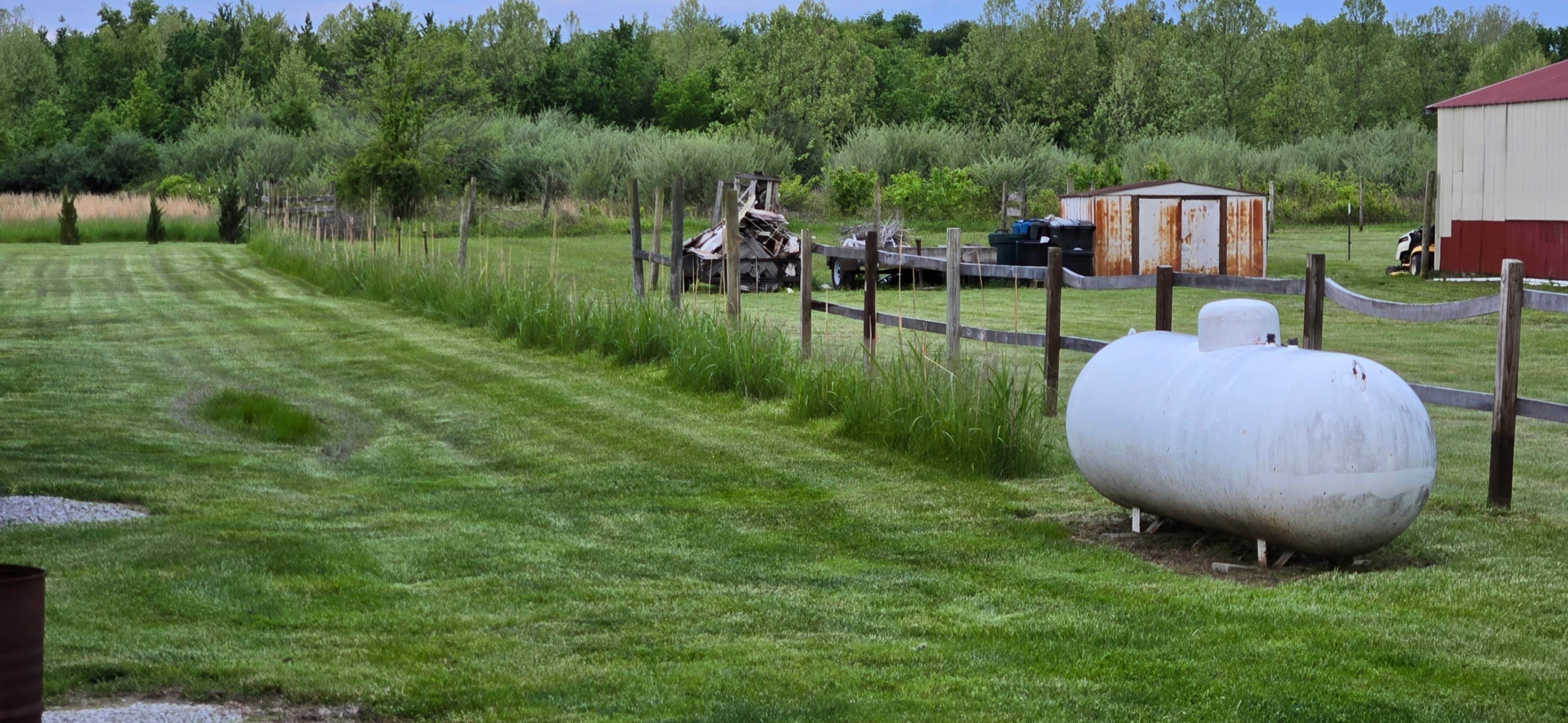 White propane tank beside rural fenced lawn